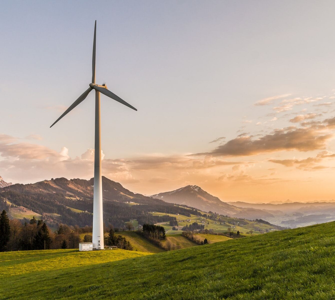 Summit Liability Solutions Wind Turbine Landscape Wind turbine on green hillside at sunset with mountains in background