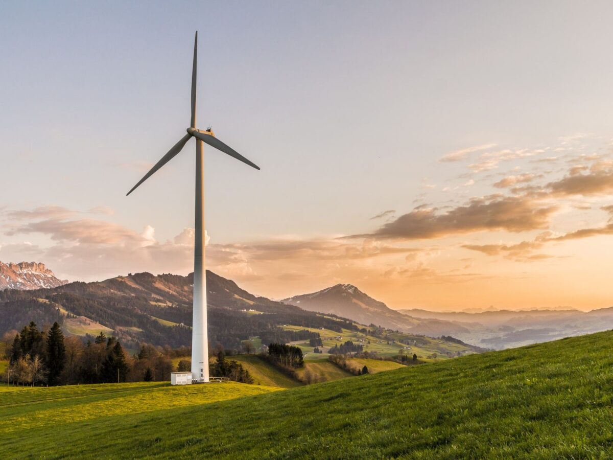 Wind turbine on green hillside at sunset with mountains in background